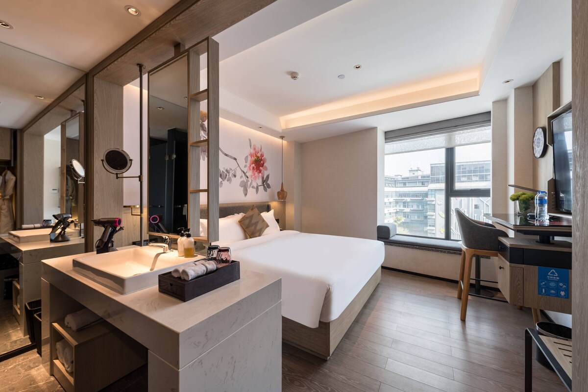 A modern hotel room with a large bed, a bathroom with a vanity, and a desk with a chair.