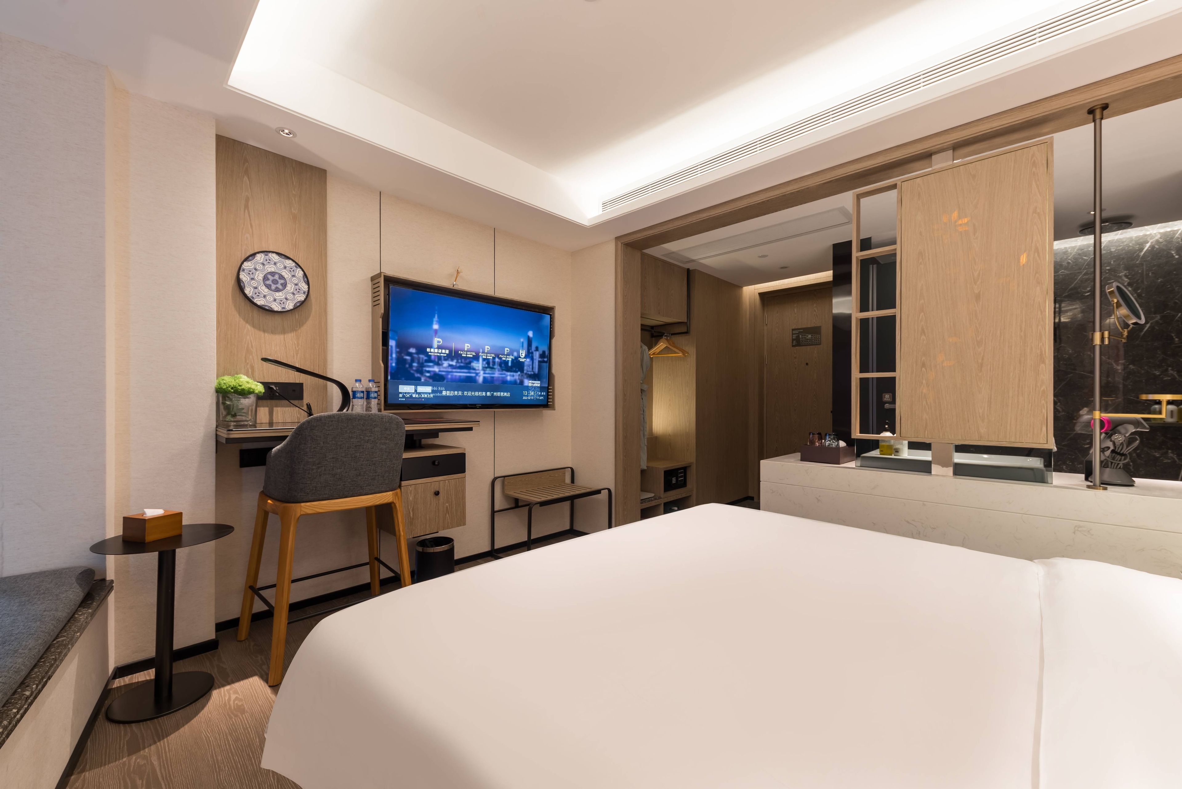 A modern hotel room with a large bed, a desk with a computer, a television, and a bathroom with a large mirror.