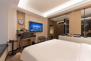 Ein modernes Hotelzimmer mit einem großen Bett, einem Schreibtisch mit Computer, einem Fernseher und einem Badezimmer mit großem Spiegel.