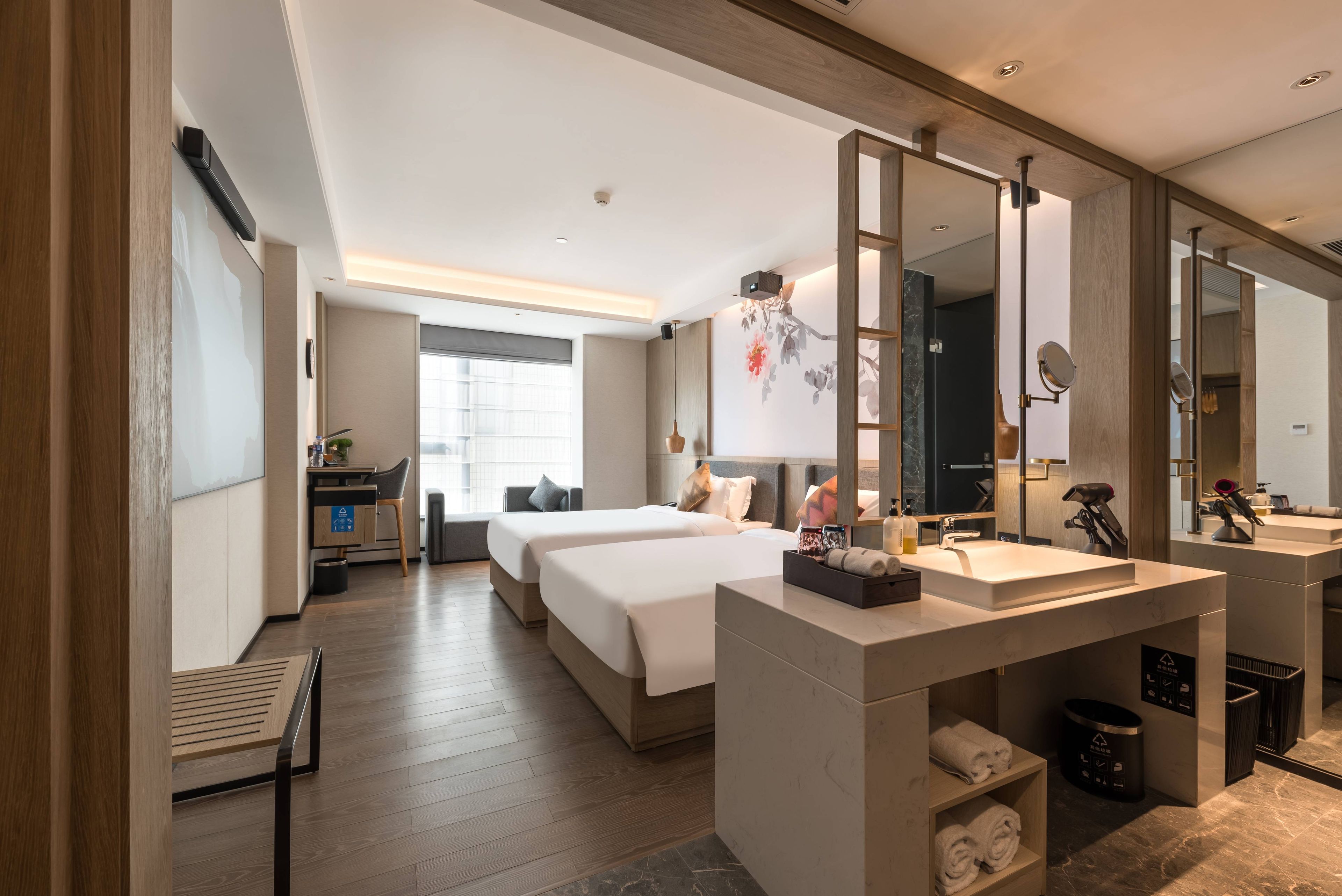 A modern hotel room with two beds, a large mirror, a vanity with a sink, and a desk with a chair.