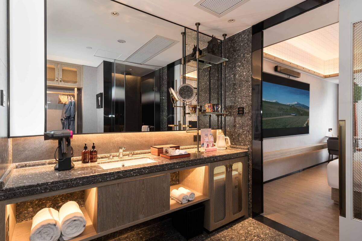 A modern bathroom with a large mirror, granite countertop, and a view of a mountain landscape through a large window.