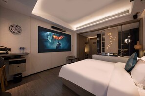 A modern hotel room with a large bed, a flat-screen TV mounted on the wall, a desk with a chair, and a small table. - Paco Hotel (Guangzhou)