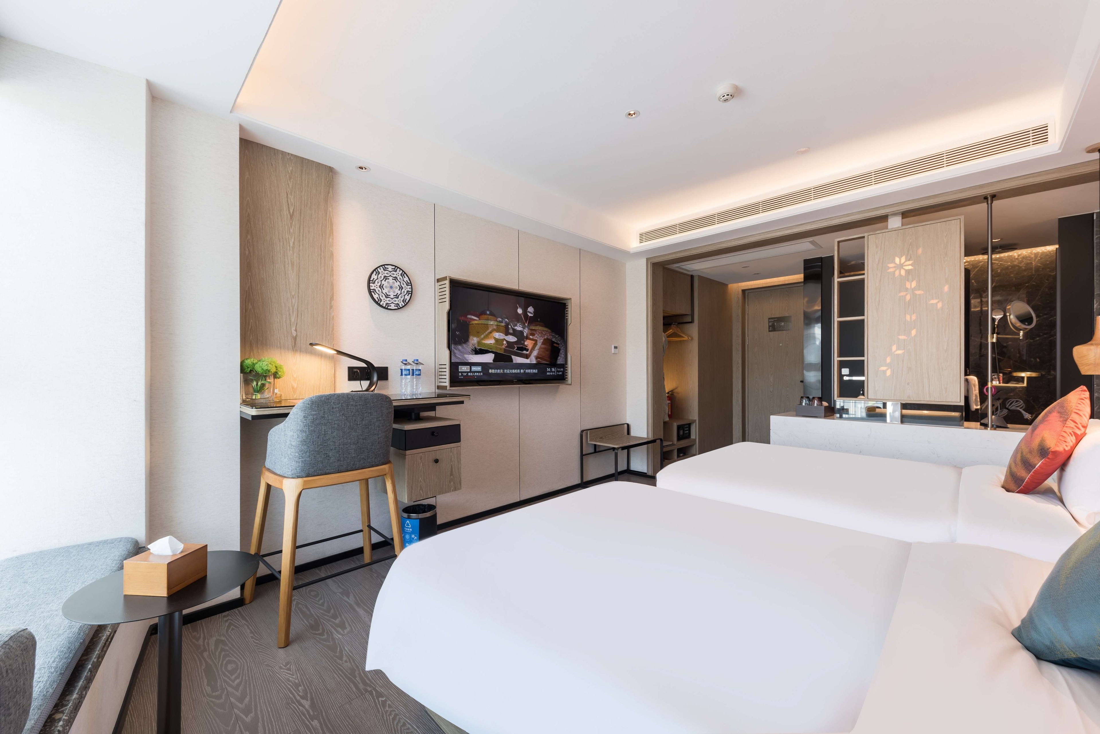 Moderni hotellihuone, jossa on suuri sänky, työpöytä tuolilla, televisio ja kylpyhuone, joka näkyy avoimesta ovesta.