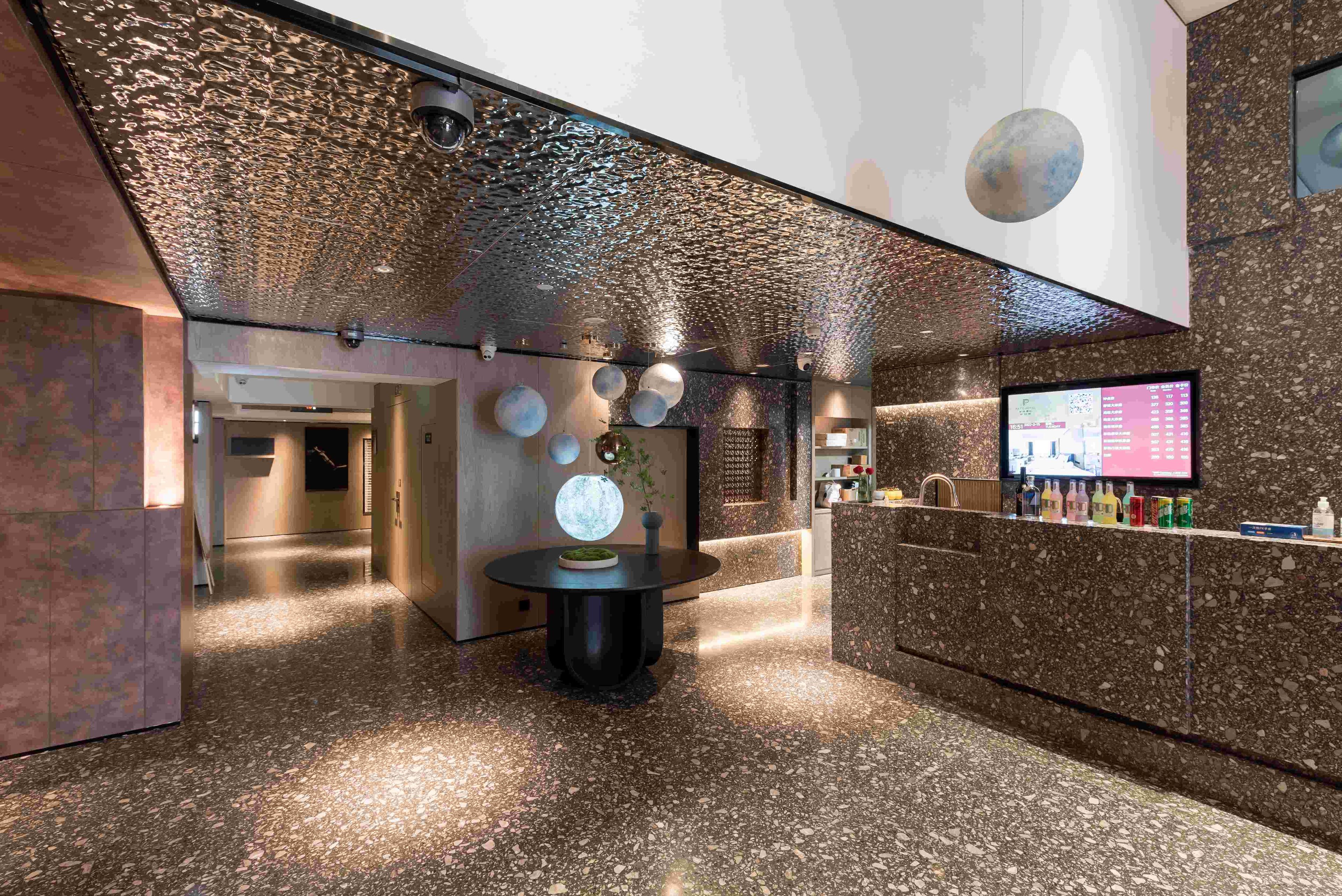 Eine moderne Lobby mit einem gefleckten Boden, einem runden Tisch mit einer Vase und einem digitalen Display an der Wand.