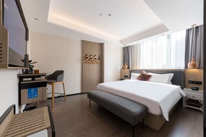 A modern hotel room with a large bed, a desk with a chair, a coat rack, and a bedside table with a lamp. - Paco Hotel (Guangzhou)