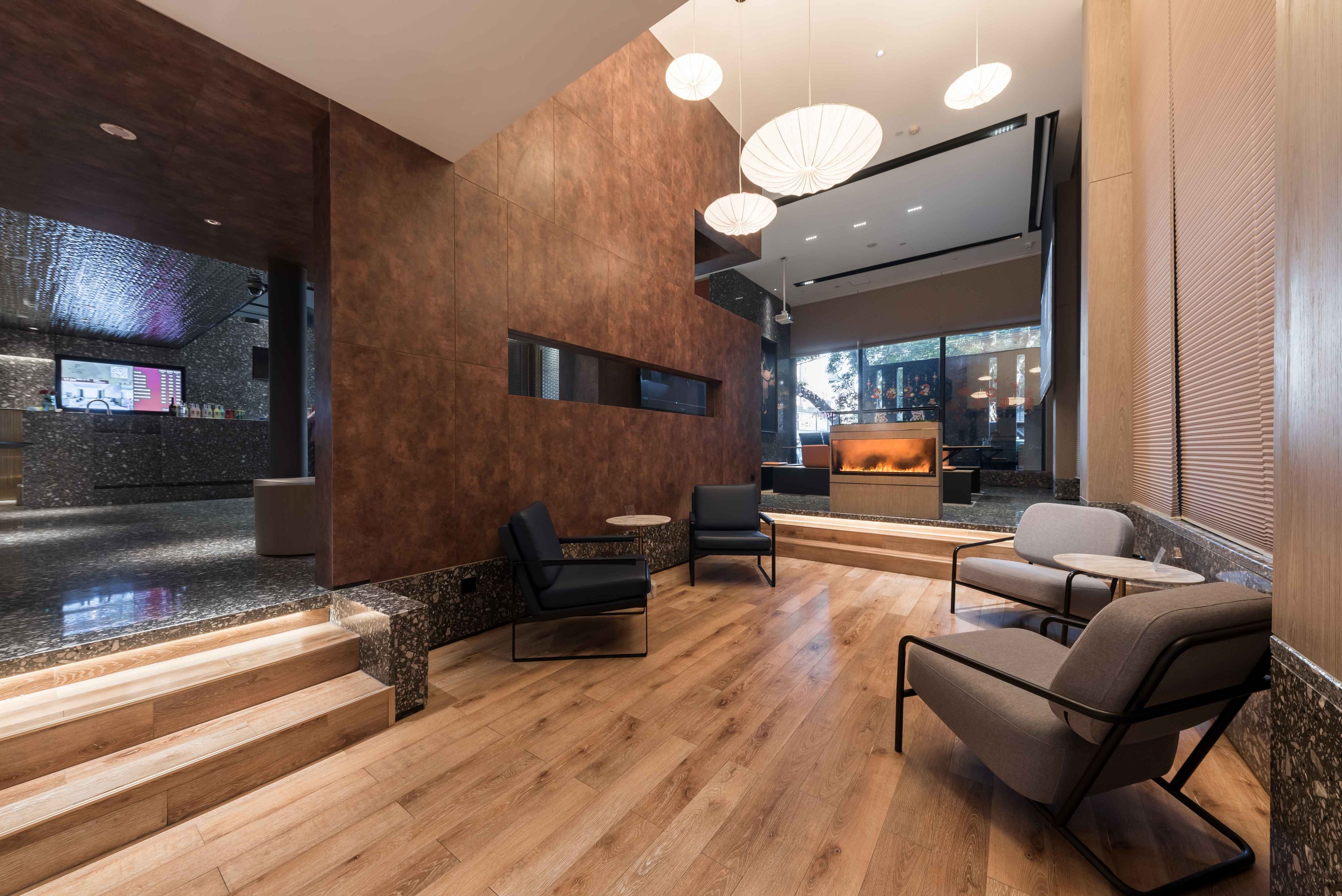 A modern lobby with wooden flooring, black leather chairs, and a reception desk.