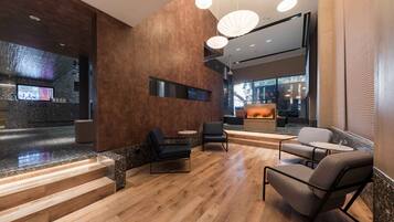 A modern lobby with wooden flooring, black leather chairs, and a reception desk.