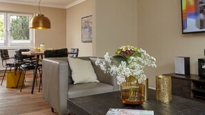 Un soggiorno moderno con un divano, un tavolino da caffè con un vaso di fiori, una zona pranzo con sedie e un'ampia finestra.