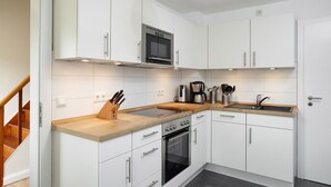 Una cucina moderna con mobili bianchi, un piano di lavoro in legno, forno integrato, microonde e macchina da caffè.