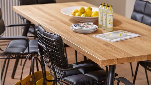 Angolo ristoro con tavolo in legno, sedie nere, una ciotola di limoni, barattoli di miele e un menu.