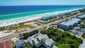 An aerial view of a coastal area with a beach, a hotel with a blue roof, and residential buildings. - 7 BR, Gulf Views, Across From Beach, Movie Theater, Pool/Spa, Discount Golf Cart (Destin)