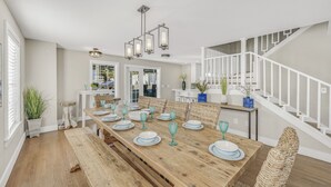 A dining area with a long wooden table set for six, white railings on a staircase, and a view of the outside. - 7 BR, Gulf Views, Across From Beach, Movie Theater, Pool/Spa, Discount Golf Cart (Destin)