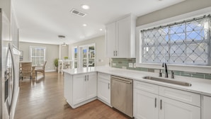 A modern kitchen with white cabinetry, a stainless steel sink, and a large window with a diamond-patterned curtain. - 7 BR, Gulf Views, Across From Beach, Movie Theater, Pool/Spa, Discount Golf Cart (Destin)
