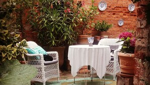 A patio with a brick wall, white wicker furniture, and potted plants.
