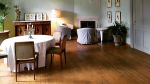 A dining room with a round table, chairs, a chandelier, a fireplace, and framed pictures on the wall.
