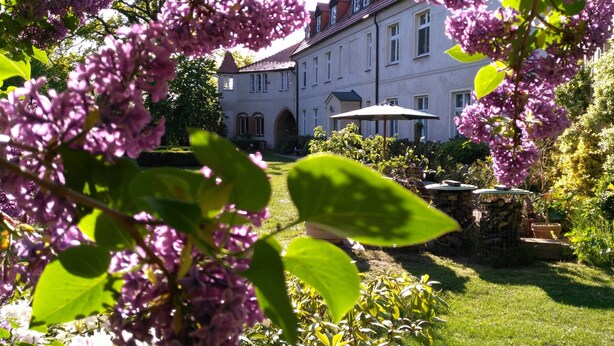A large building with a garden in front, including a lawn and a patio area with an umbrella.