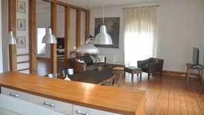 A modern kitchen with wooden countertops, a dining area with a table and chairs, a sofa, and a television.