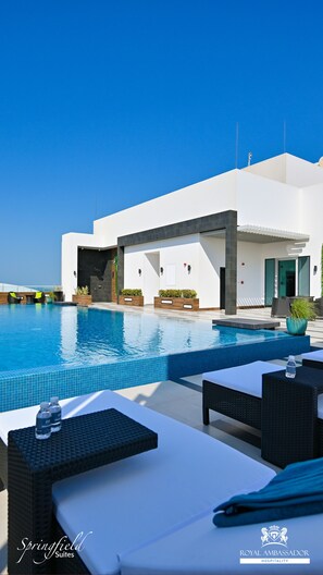 A modern hotel with a pool, outdoor seating, and a clear view of the sky. - Springfield Suites (Manama)