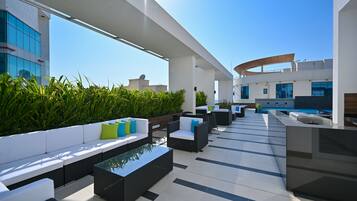 A rooftop lounge with outdoor seating, a pool, and modern architecture.