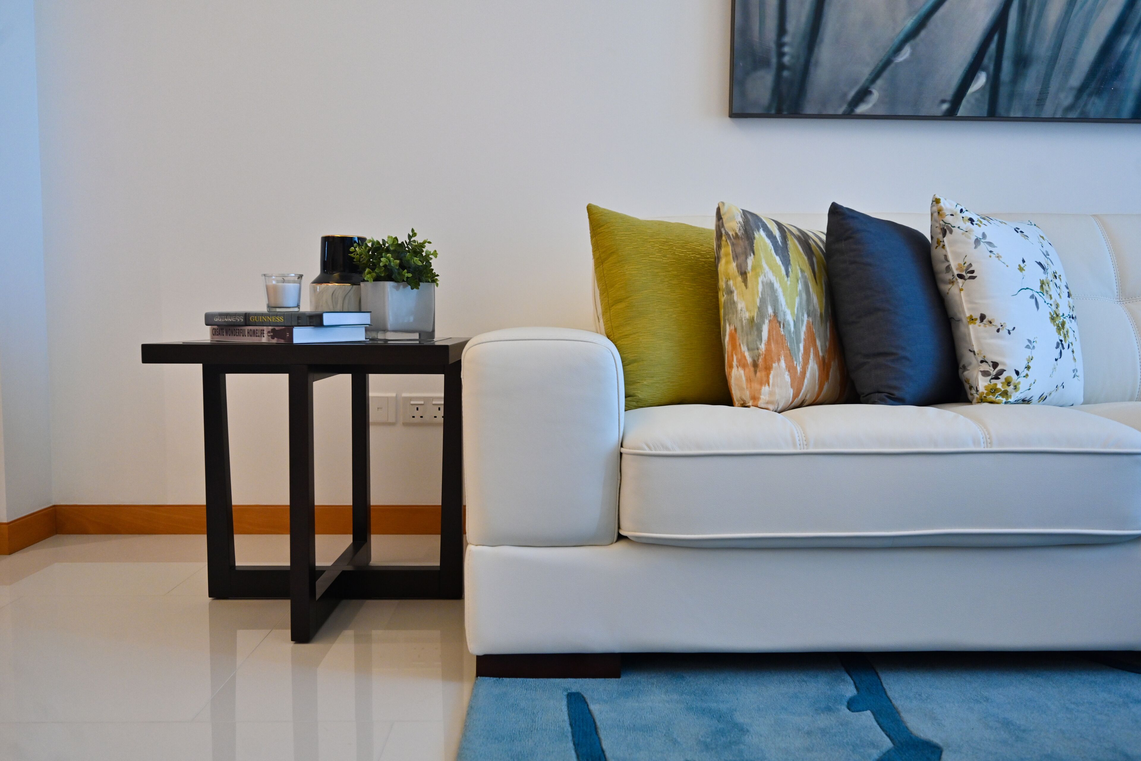 A modern living room with a white sofa, a black side table, and a blue rug.