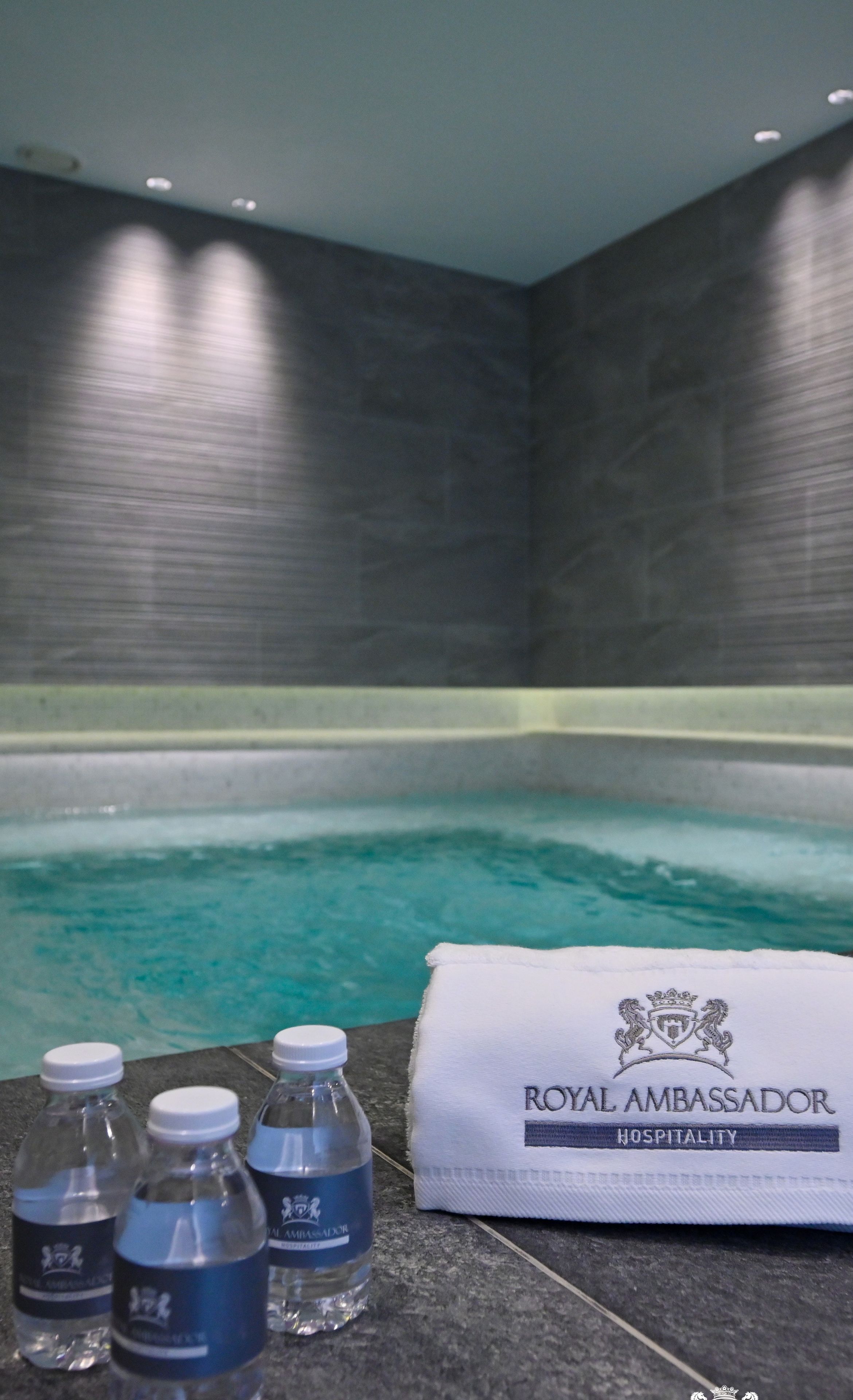 A spa area with a pool, a towel, and bottled water labeled 'Royal Ambassador Hospitality'.