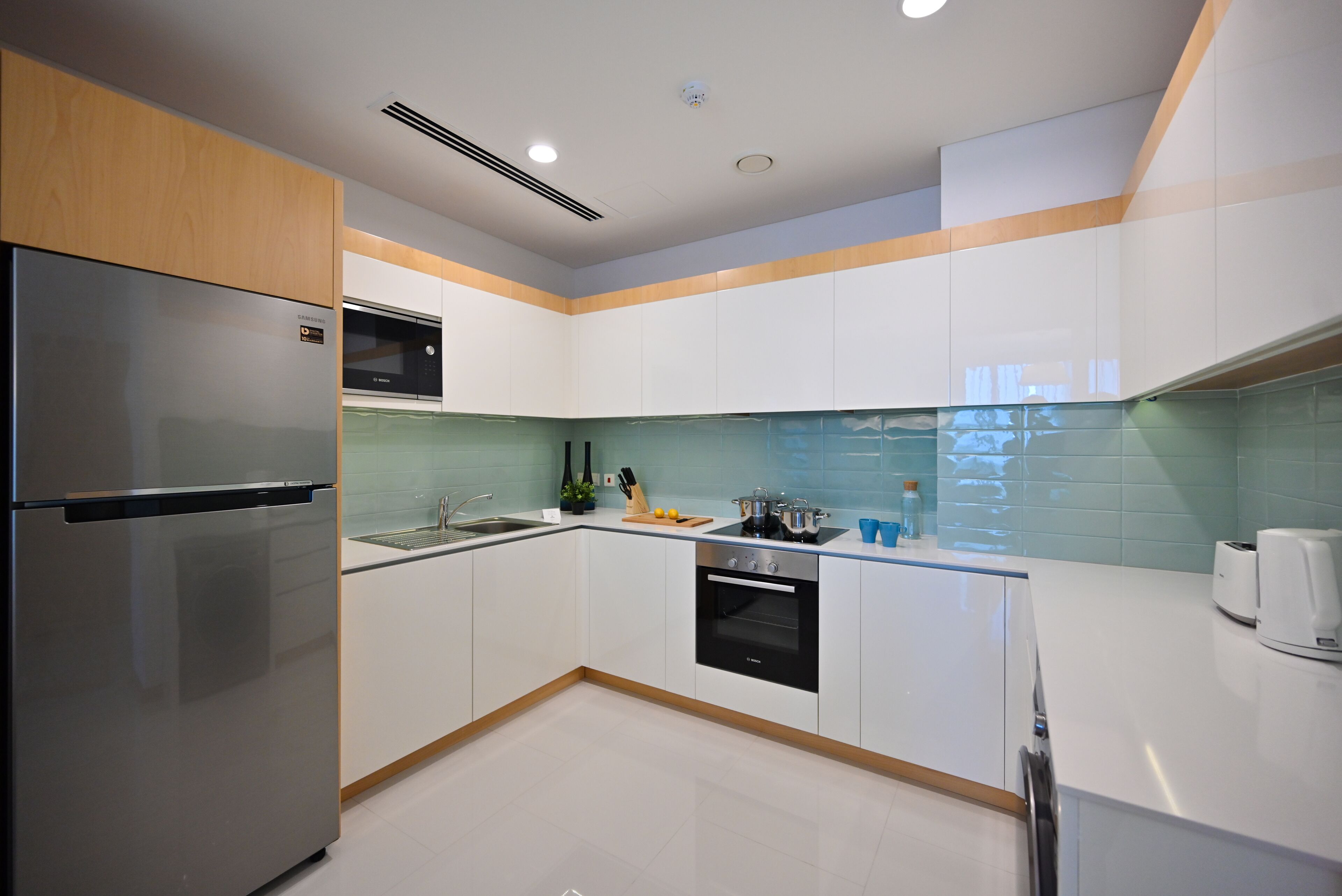 A modern kitchen with white cabinets, a stainless steel refrigerator, a microwave, and a built-in oven.