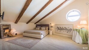 A bedroom with a sloped ceiling, a bed, a nightstand, a mirror, a framed artwork, and a small table with a lamp.