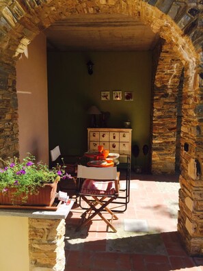 An outdoor dining area with a stone archway, a table set with plates and a potted plant.