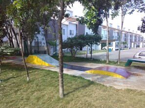 A playground with a yellow and purple slide, surrounded by trees and a fence.