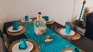 Una mesa de comedor dispuesta con servilletas color turquesa, vasos transparentes y un centro de mesa decorativo.