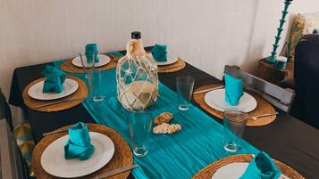 Una mesa de comedor dispuesta con servilletas color turquesa, vasos transparentes y un centro de mesa decorativo.
