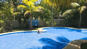 Una piscina con borde de baldosas, rodeada de palmeras y un letrero.