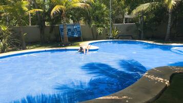 Una piscina con borde de baldosas, rodeada de palmeras y un letrero.