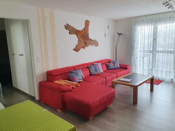 Un salon avec un canapé rouge, une table basse, une table verte et un élément de décoration murale en bois.
