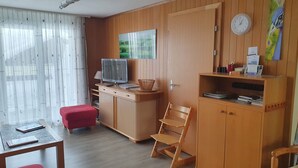 A room with a wooden desk, a television, a red chair, and a bookshelf. - Elfe - Apartments Three-bedroom Apartment for 6 Guests With Patio (Emmetten)