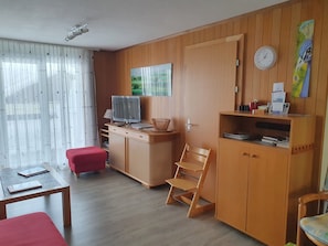 A room with a wooden desk, a television, a red chair, a wooden cabinet, and a clock on the wall.