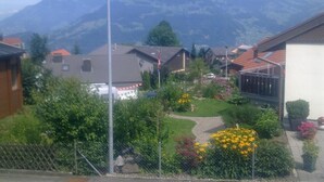 A residential area with houses, a garden with flowers, and mountains in the background. - Elfe - Apartments Three-bedroom Apartment for 6 Guests With Patio (Emmetten)