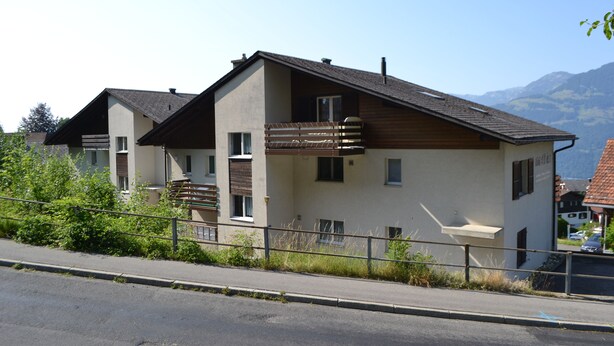 A modern two-story building with a balcony, a visible window, and a mountain backdrop. - Elfe - Apartments Three-bedroom Apartment for 6 Guests With Patio (Emmetten)