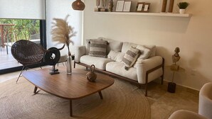 Un salon moderne avec un canapé, une table basse ronde, un fauteuil en osier et un luminaire suspendu.