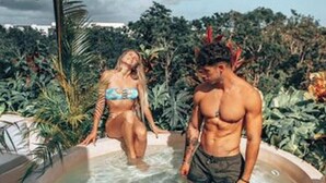 Un bain à remous où se trouvent deux personnes, entouré d’une végétation luxuriante et sous un ciel nuageux.