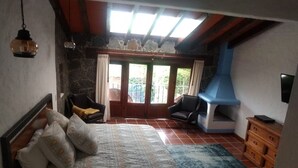 Une chambre à coucher comprenant un lit, deux chaises, une commode en bois, une cheminée et une vue sur l’extérieur, visible à travers une porte vitrée.