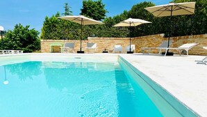 A swimming pool with clear blue water, surrounded by white lounge chairs and beige umbrellas.
