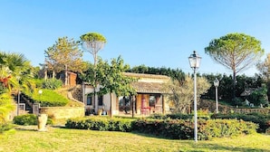 A villa with a terracotta roof, surrounded by lush greenery and a stone wall.
