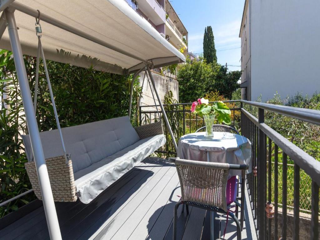 Ein Balkon mit bequemen Sitzgelegenheiten, einem kleinen runden Tisch und einer Blumenvase, sowie einem Metallgeländer.