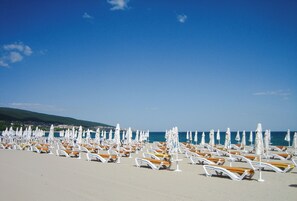 A beach with rows of sun loungers and umbrellas, a clear sky, and a distant view of a town. - Seaside Apartment With 2 Bedrooms for up to 5 Guests (Nessebar)