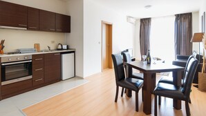A modern kitchen with wooden cabinets, a dining table with chairs, and a view of the living area through a doorway. - Seaside Apartment With 2 Bedrooms for up to 5 Guests (Nessebar)