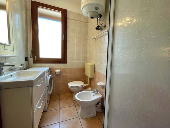 Une petite salle de bain comprenant un lavabo, un lave-linge, des toilettes, un bidet et une fenêtre.