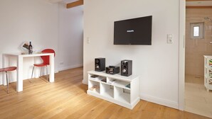 A modern living room with a flat-screen TV, wooden beams on the ceiling, a white entertainment unit with speakers, and a red chair. - Birklund - Holiday home for two (Sankt Peter-Ording)