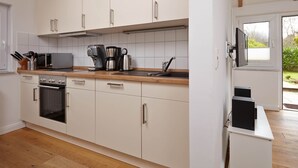A modern kitchen with white cabinets, a built-in oven, a microwave, and a coffee maker. - Birklund - Holiday home for two (Sankt Peter-Ording)