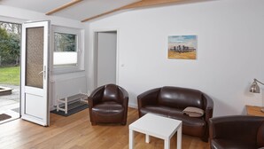 A modern living room with a brown leather sofa, a white coffee table, and a painting on the wall. - Birklund - Holiday home for two (Sankt Peter-Ording)